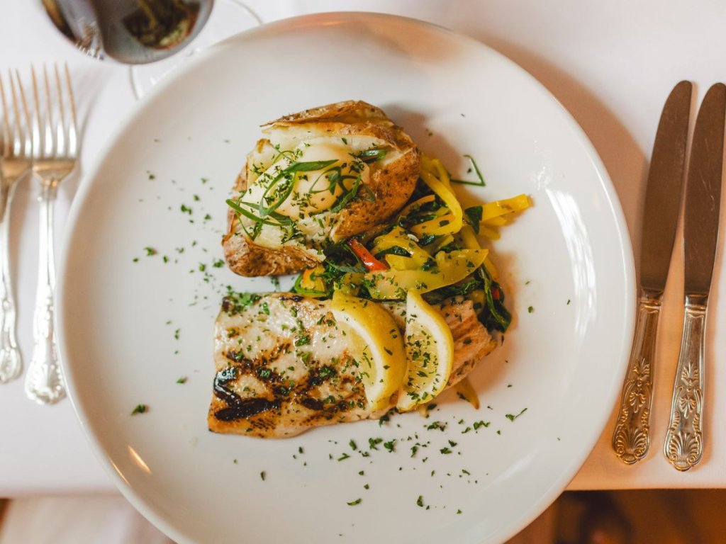 Grilled fish fillets topped with herbs and lemon, served with colorful saut&eacute;ed vegetables on a white plate at the General Lewis in Lewisburg, WV.
