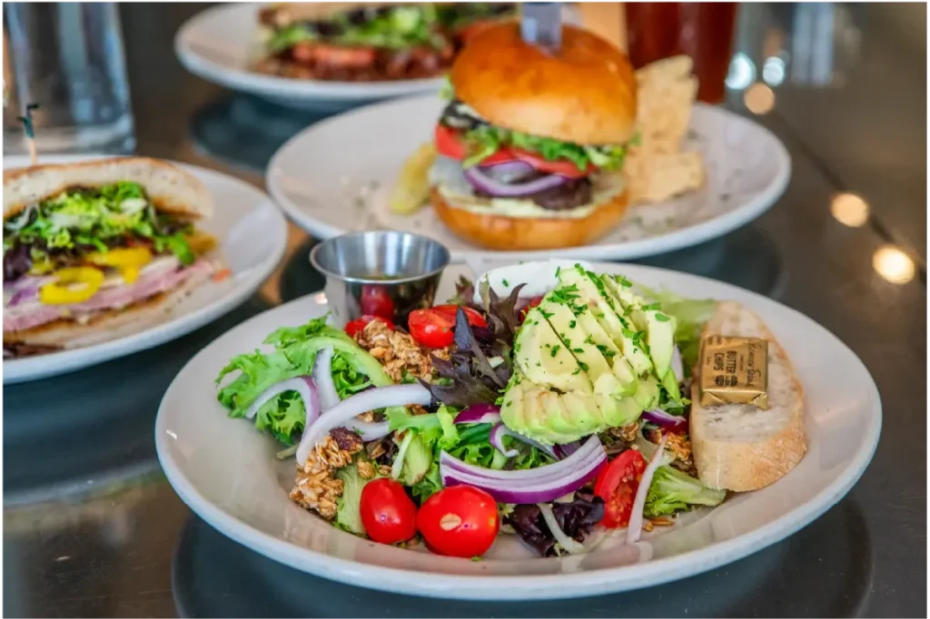 The "Trust Me" salad at Stardust Cafe in Lewisburg, West Virginia. A vibrant salad with mixed greens, cherry tomatoes, and avocado, accompanied by a burger and sandwich in the background.